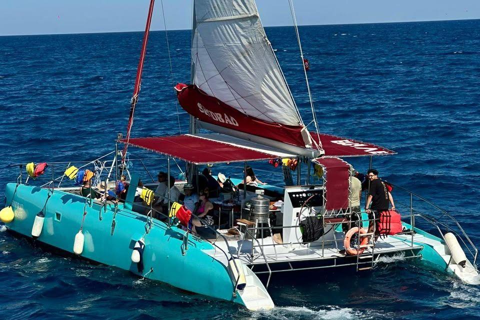 Under sail on the open sea, passengers shaded by the red awning